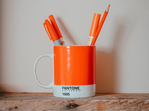 Eine Tasse im Design einer Pantone Farbkarte in Orange mit orange-farbenen Stiften