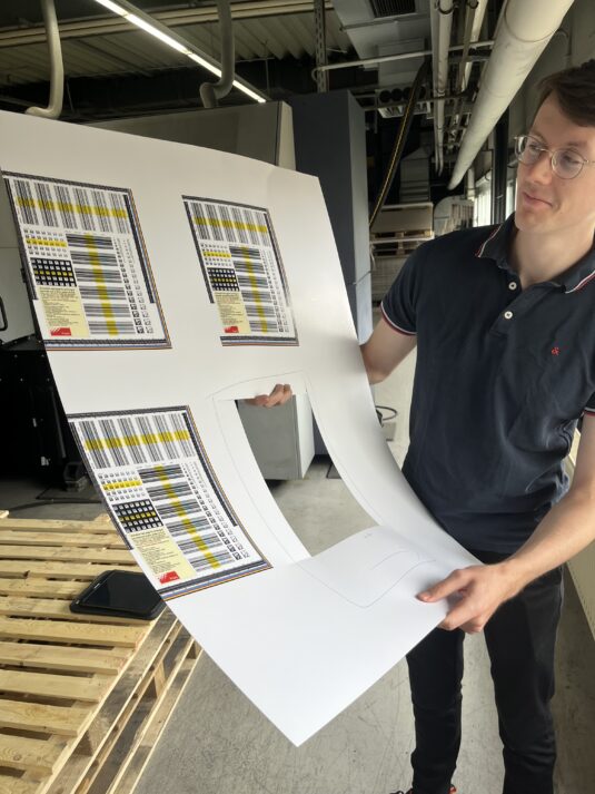 Fogra-Mitarbeiter Dr. Moritz Feil zeigt den Einfluss von optischen Aufhellern. Während der Bedruckstoff im unteren Teil bläulicher wirkt (viel UV), ist er im oberen Bereich gelblicher (weniger UV).